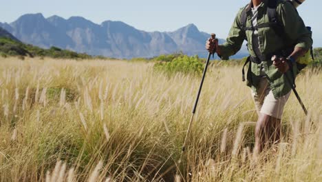 hombre afroamericano haciendo senderismo con palos de senderismo en el campo montañoso