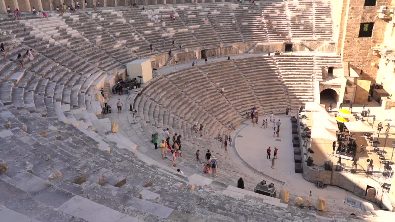 A distant view of the ancient theater in the afternoon, with tourists walking back and forth