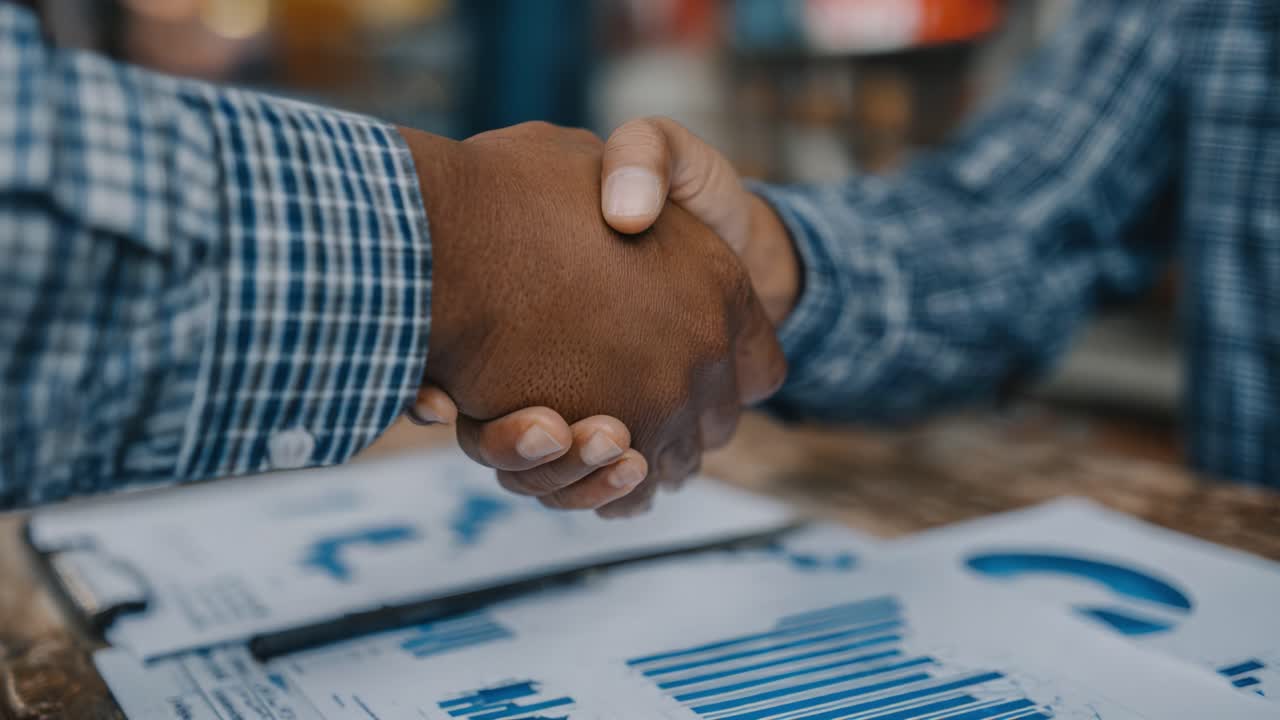 A Professional Handshake Between Two Individuals Marking Successful Collaboration and Agreement in a Business Environment Surrounded by Data Reports and Graphs