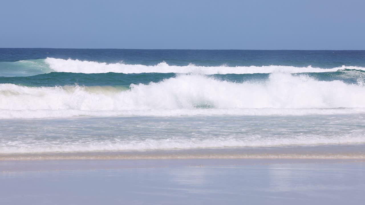 모래 해변에 굴러가는 연속적인 바다 파도