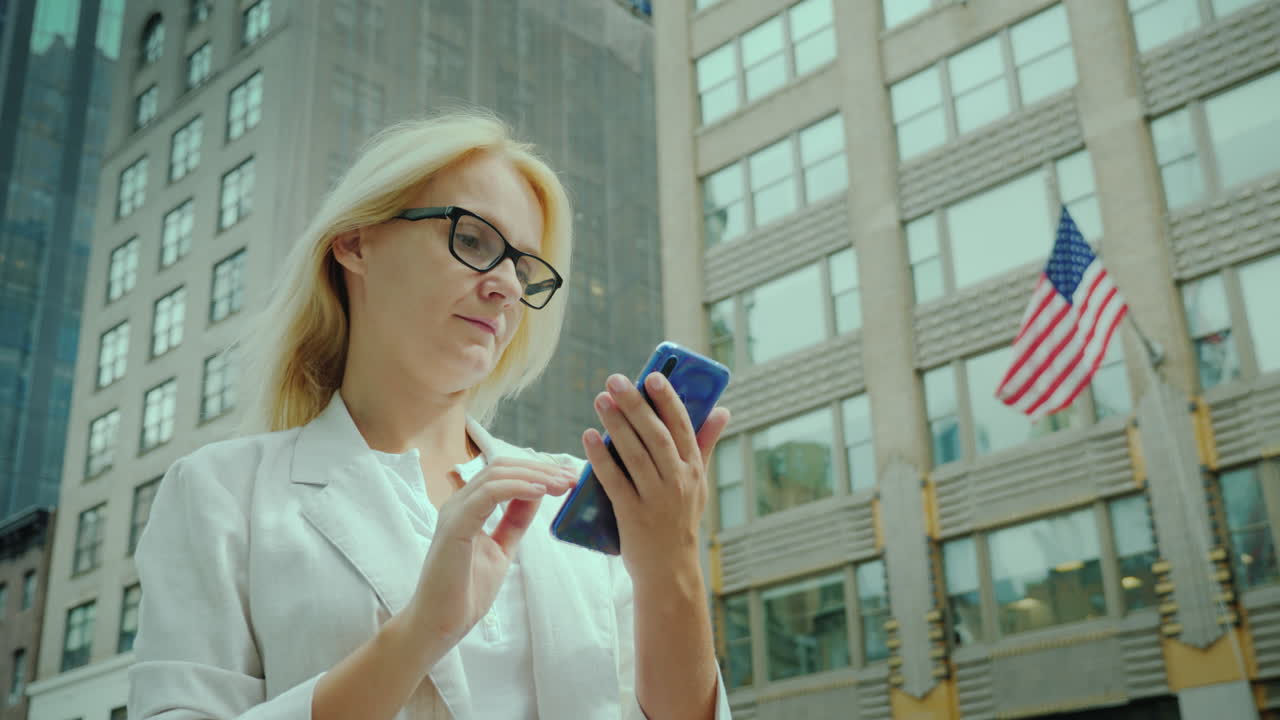 사업가는 사무실 건물 배경에 뉴욕 거리에서 스마트폰을 사용합니다.