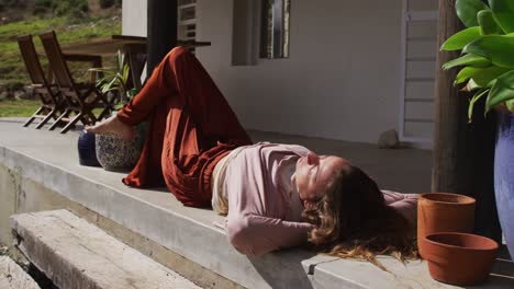 happy caucasian woman lying in the sun, relaxing with eyes closed on cottage terrace