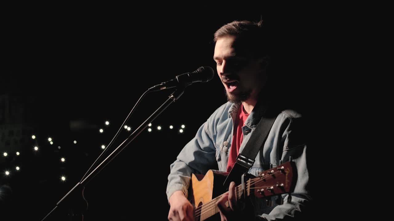 un músico está tocando la guitarra en un gran escenario con miembros de la audiencia sosteniendo linternas en el fondo. el auditorio está lleno de hermosas luces parpadeantes.