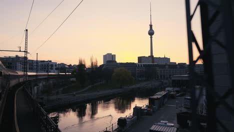 Driving-with-train-over-a-river-bridge-in-Berlin,-Germany-at-sunset-with-view-on-television-tower-copy-space,-sunrise,-fernsehturm