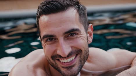 handsome man with short brown hair and a beard enjoys a relaxing time in a swimming pool, his genuine smile reflecting happiness and contentment