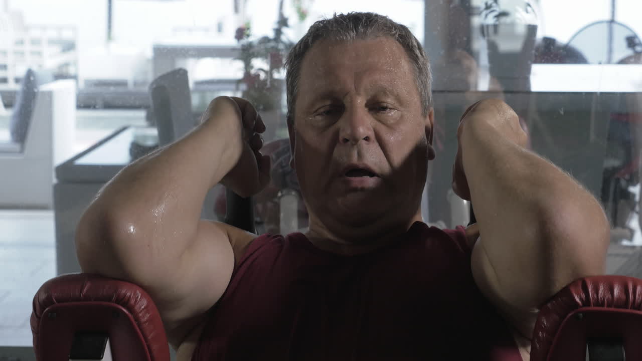 Hombre cansado y sudoroso entrenando en una máquina de fitness.