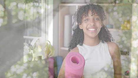 animation of trees over happy biracial teenage girl holding yoga mat