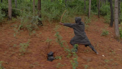 Aerial-shot-tracking-an-African-hunter-from-the-side-as-he-walks-through-the-bush-takes-aim-and-shoots-a-wooden-bow-an-arrow