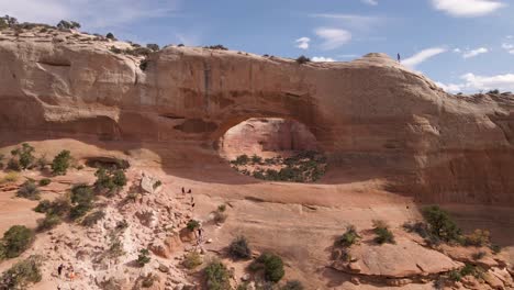 group of travelers climbing the amazing red rock formation known as wilson arch, a roadside attraction in moab, utah, united states - wide shot pan left