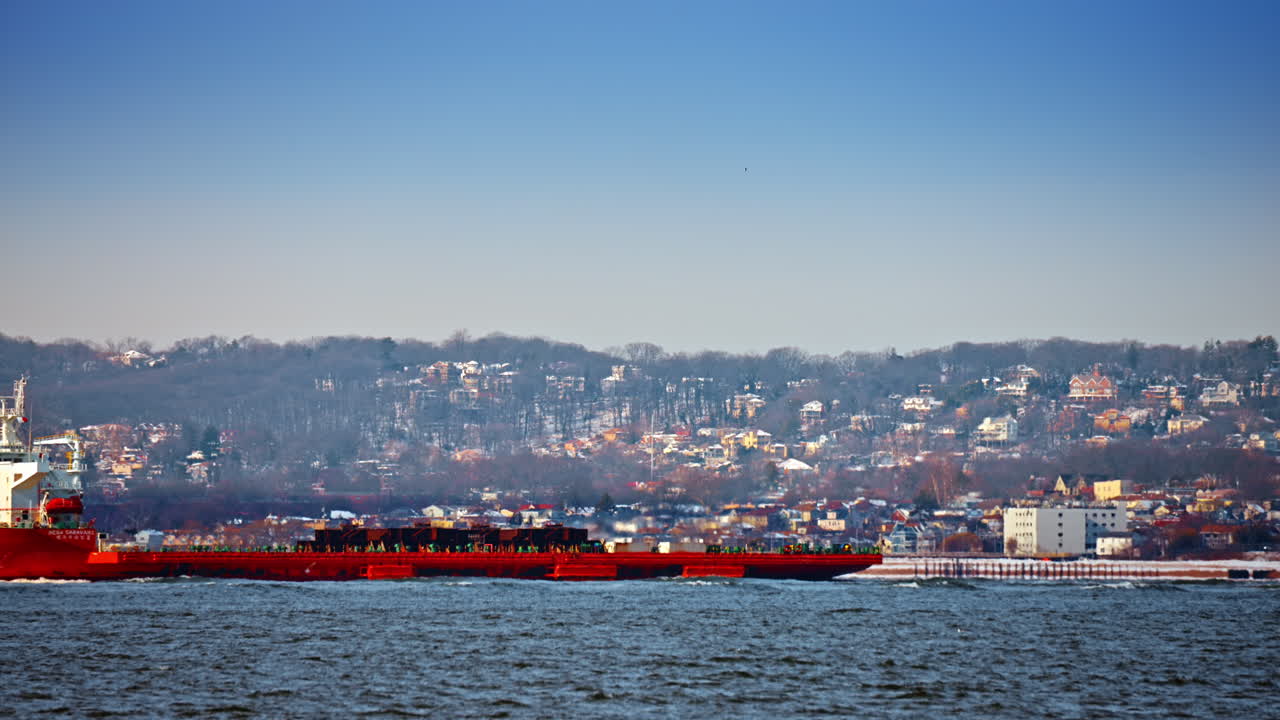 New York, USA, 25 dicembre 2025: Nave da carico industriale rossa che naviga lungo la costa innevata. Una grande nave portarinfuse rossa che naviga in acque vicine a colline coperte di neve.