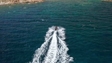 A-speedboat-cruises-through-the-deep-blue-waters-off-the-coast-of-Sardinia,-aerial-view