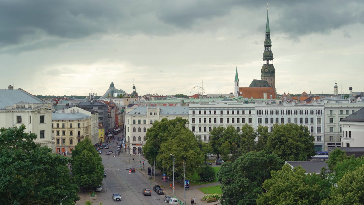Traffico stradale della Città Vecchia di Riga sotto un cielo tempestoso cupo e coperto con la storica guglia della Chiesa di San Pietro sullo sfondo. Con vista sullo skyline della città