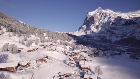 empujando sobre el pueblo de montaña cubierto de nieve de grindelwald en dirección al monte wetterhorn en un día de invierno de pájaro azul