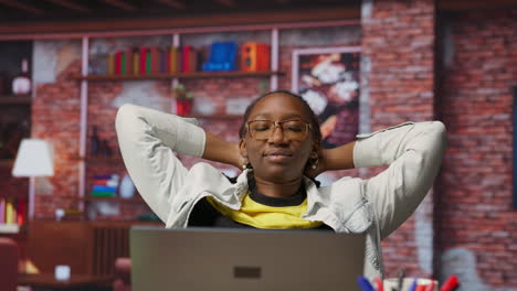 joyous woman relaxing at home, sitting back and watching tv show on laptop