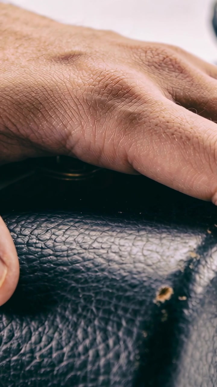 Video vertical: Mano adulta probando una superficie de cuero negro desgastado en primer plano, mostrando un desgarro amarillo.