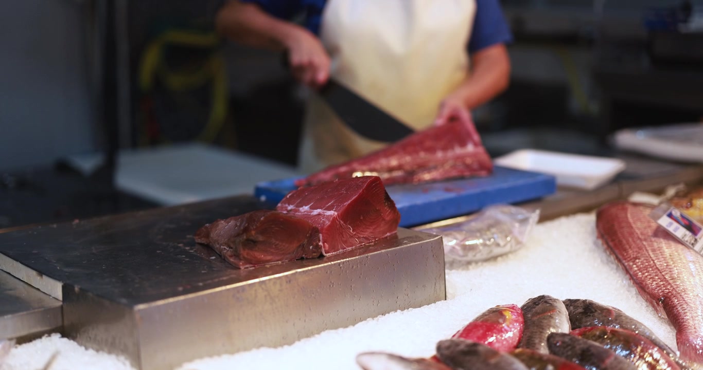Poissonnier découpant un filet de thon frais sur un marché aux poissons