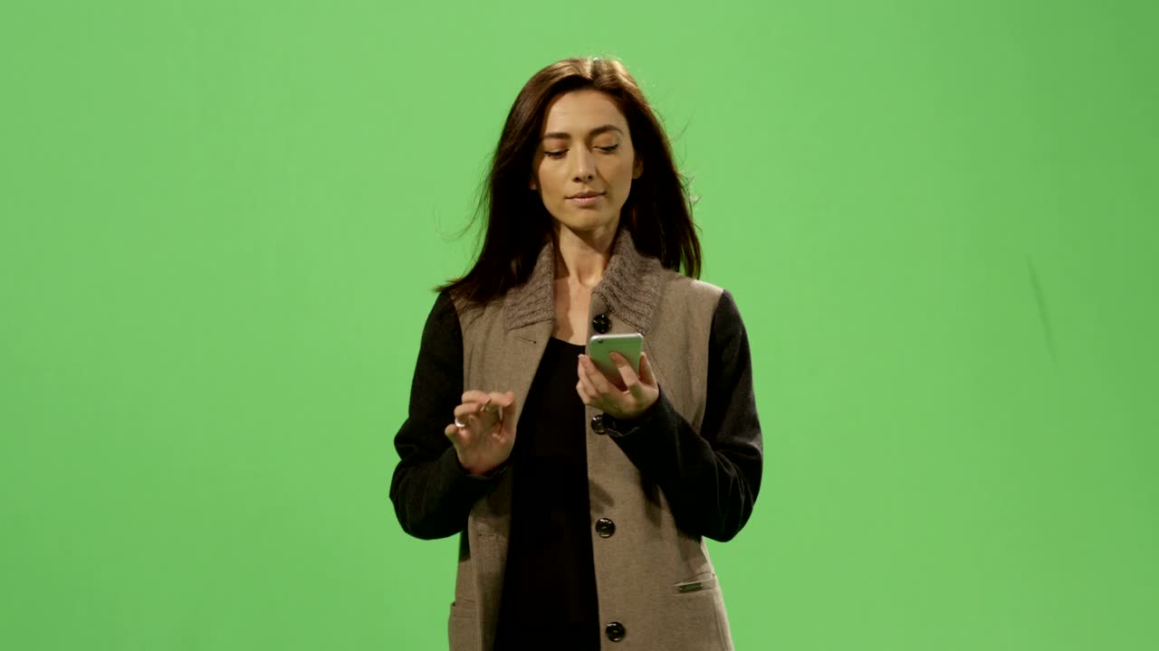 Casual brunette female is walking and using a smartphone on a mock-up green screen in the background.