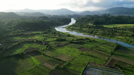 orbiting aerial view of picturesque provincial farmlands and rice paddies with winding river and lush mountains