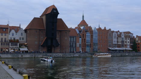 riverside view of crane zuraw at gdansk poland historical building , boat passes by and people walking by the shore , day shot