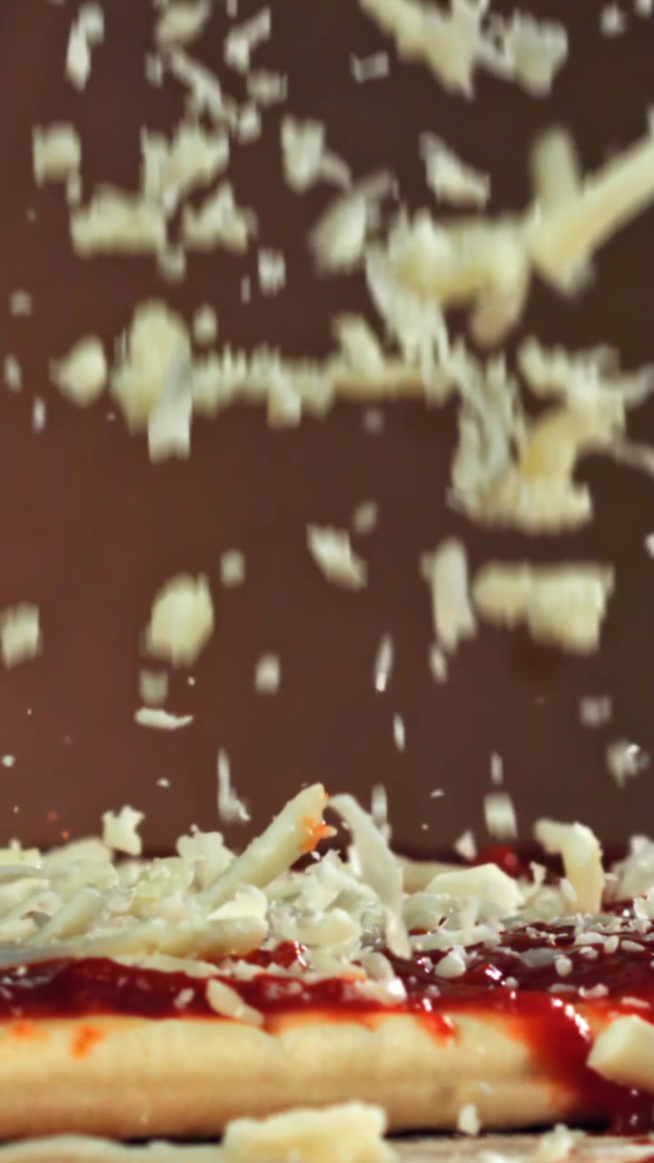 Shredded Cheese Falling onto Pizza with Tomato Sauce in Slow Motion
