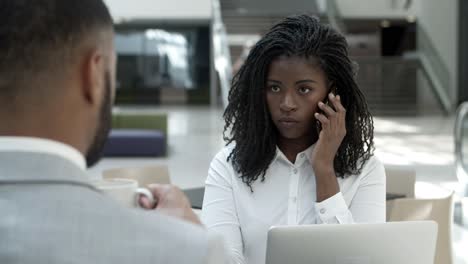 serious woman talking on smartphone and looking at colleague