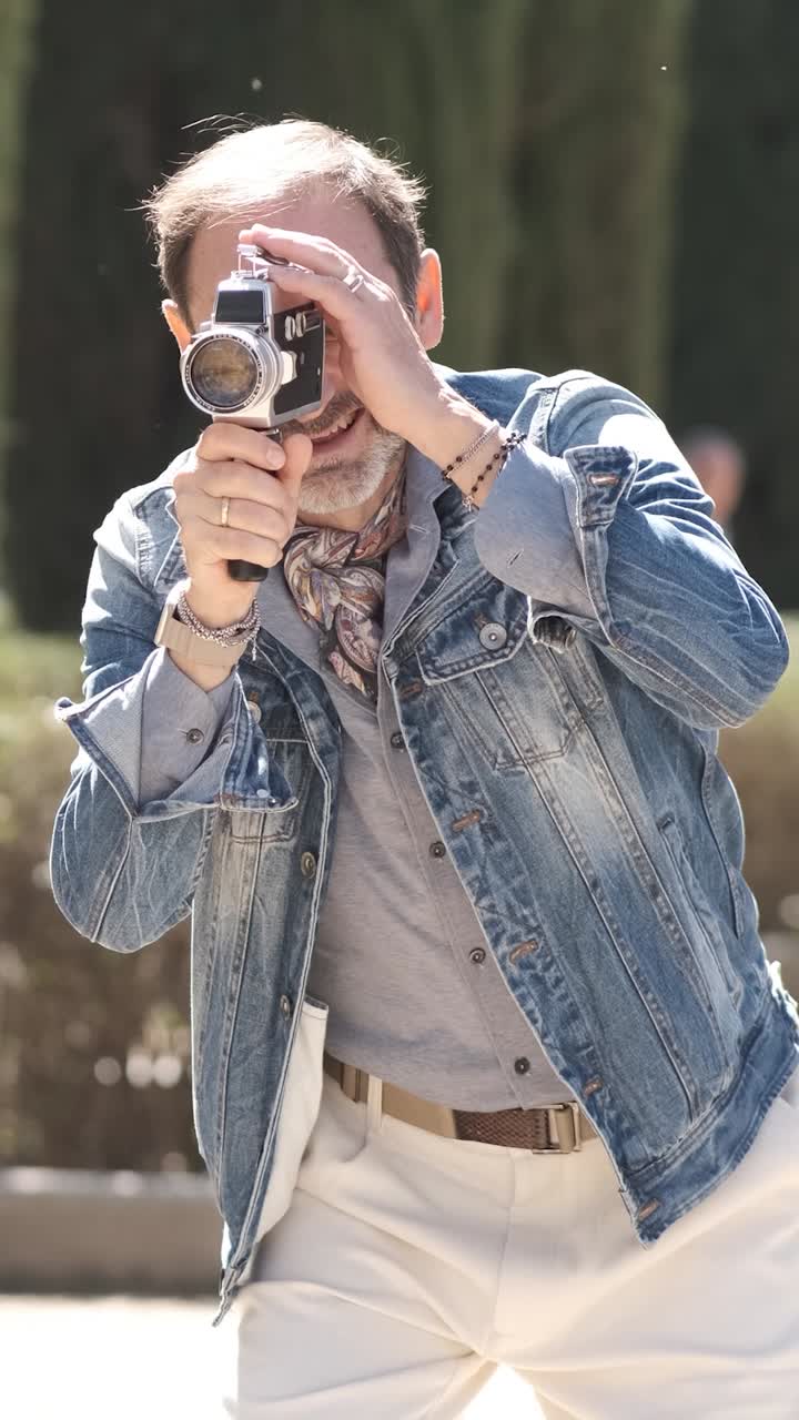 Uomo maturo che gira un video in un parco cittadino con una macchina fotografica vintage. Filmato verticale.