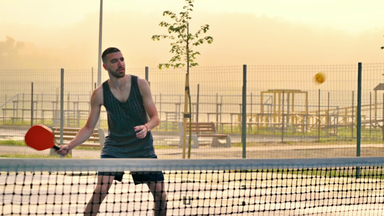 Man playing pickleball with a red racket at sunrise, after rain