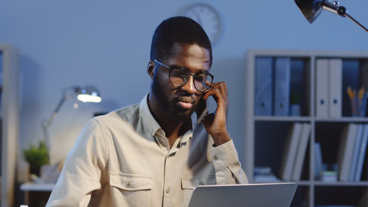 Portrait Of Young Office Worker Sitting At Desk And Talking On The Phone In The Office At Night