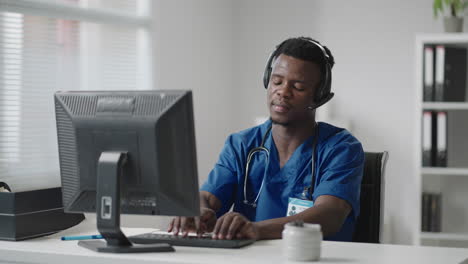 a black man sits at a computer in a doctor's uniform and writes a patient's card while taking calls with headphones. ambulance hotline receive calls and distribute ambulances