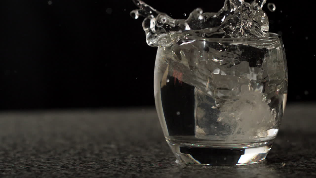 Cubetto di ghiaccio che cade nel bicchiere d'acqua