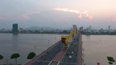 Aerial-spinning-around-Dragon-Bridge-Cau-Rong,-traffic-and-city-skyline-during-sunset-in-Danang,-Vietnam