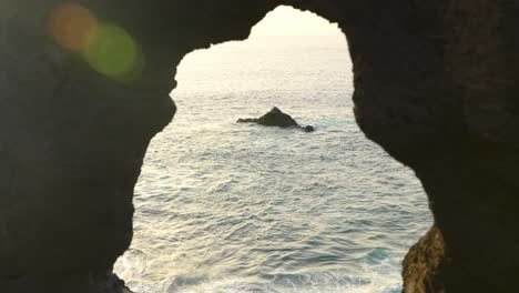 waves engulf small rock island, framed by cave entrance