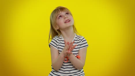 a young girl with blonde hair smiles and poses in a striped shirt against a yellow background