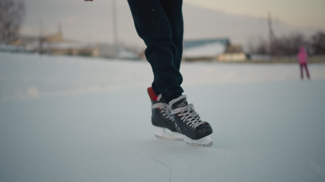 experienced skater gliding across ice rink with another skater visible in blurred background, winter evening light casting soft glow on smooth frozen surface
