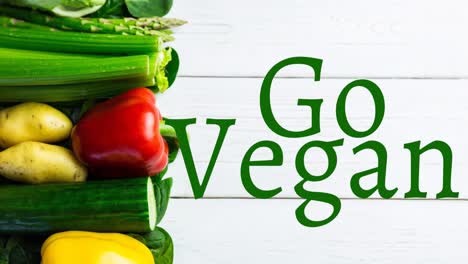 Animation-of-go-vegan-text-in-green-over-fresh-vegetables-on-white-boards