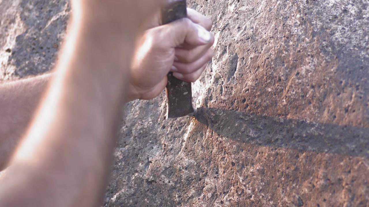 Person Using Chisel and Stone to Carve Rock Surface