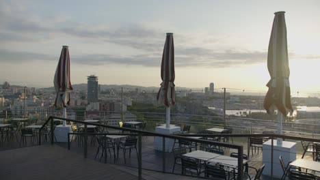 Vista-De-La-Cornisa-Del-Café,-Horizonte-De-La-Ciudad-De-Barcelona-España-Con-Amanecer-Dorado-En-6k-Mientras-Los-Pájaros-Vuelan