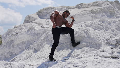 handsome bodybuilder posing on camera. sportive african american man in black glasses without shirt showing his strong muscles against white hill.