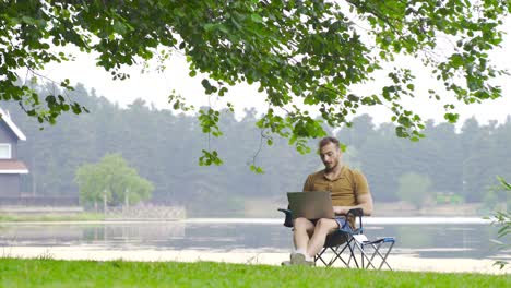 man working with computer by lake in nature.