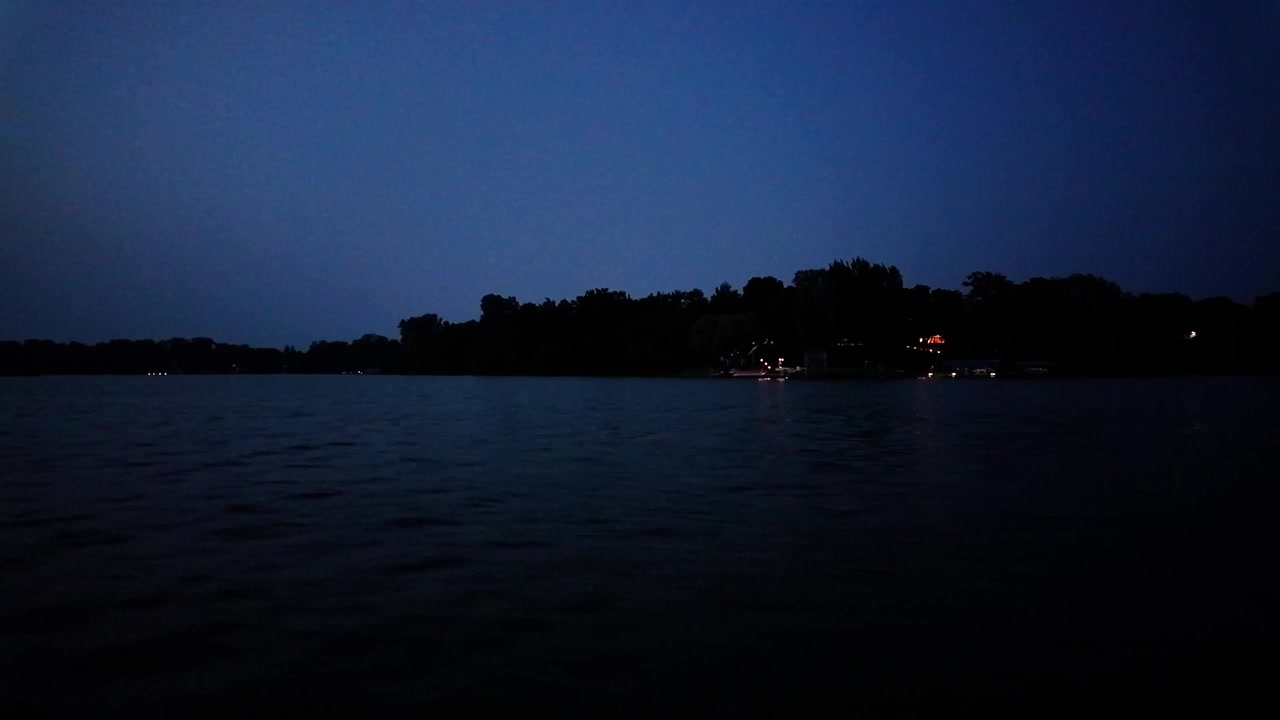 Ripresa panoramica con gimbal da una barca in movimento che passa accanto a cabine sul lago di notte a Center Lake, Minnesota. 4K.