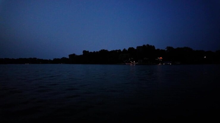 Ripresa panoramica con gimbal da una barca in movimento che passa accanto a cabine sul lago di notte a Center Lake, Minnesota. 4K.