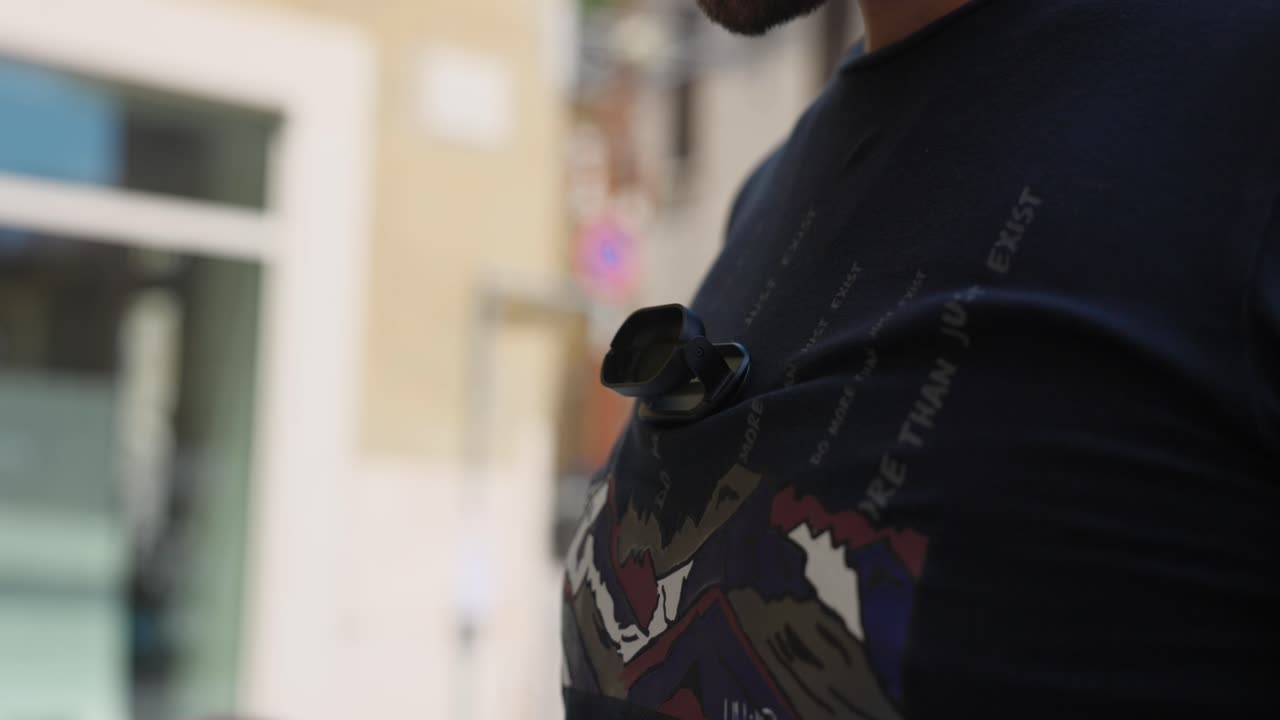 Close-up of a person wearing a graphic t-shirt with 'Do More Than Just Exist' and a small body camera