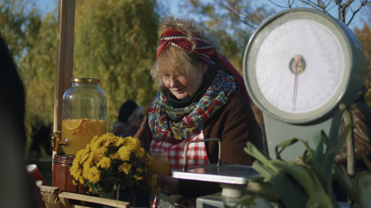 Elderly Saleswoman Stands at the Stall Elderly Saleswoman Stands at the Stall Gives Honey to Taste People Pay for a Jar of Honey with Cash Local Farmers Market or Autumn Fair Outdoors Vegetarian and Organic Food Agriculture