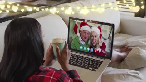 Lichterketten-über-Einer-Frau-Mit-Einer-Kaffeetasse,-Die-Zu-Weihnachten-Einen-Videoanruf-Auf-Dem-Laptop-Führt