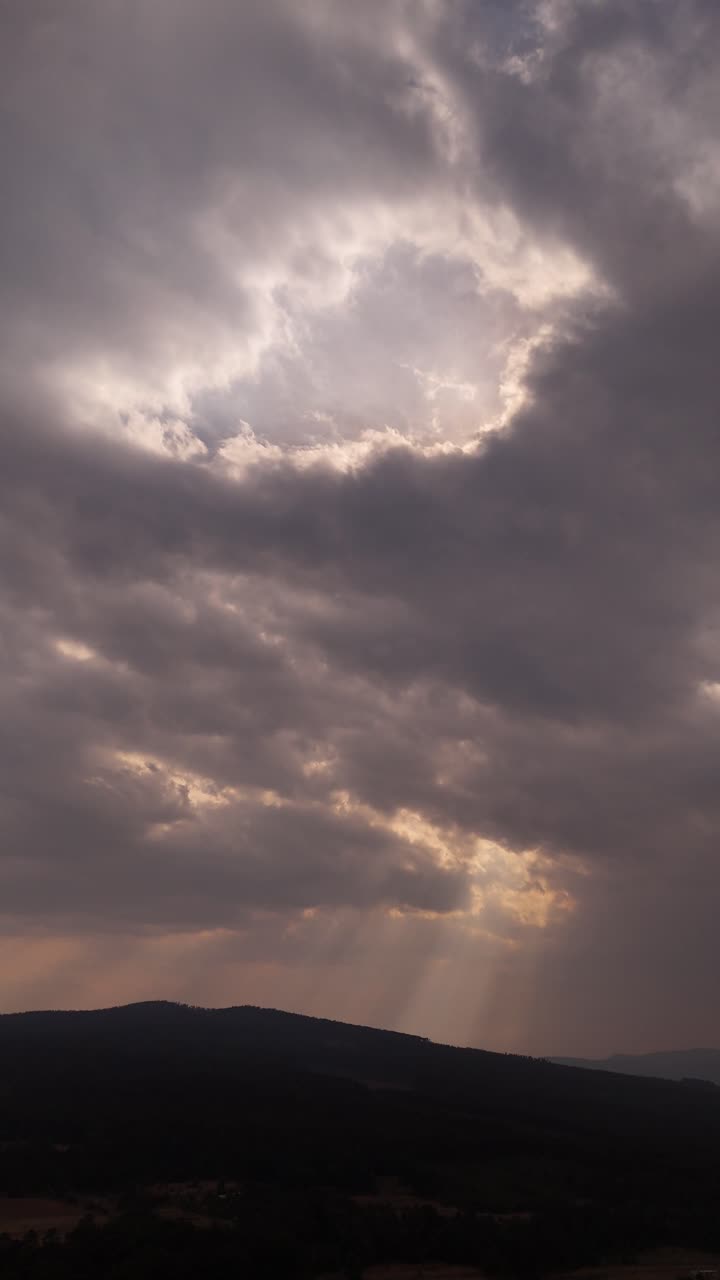 A breathtaking cloudy sky with a few rays of sunshine piercing through and reaching the mountains.