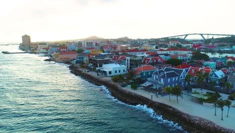 Vista-Aérea-De-La-Puesta-De-Sol-De-La-Hora-Dorada-De-4k-De-La-Ciudad-De-Willemstad,-El-Distrito-De-Pietermaai-Y-El-Puente-De-La-Reina-Juliana-En-Curazao