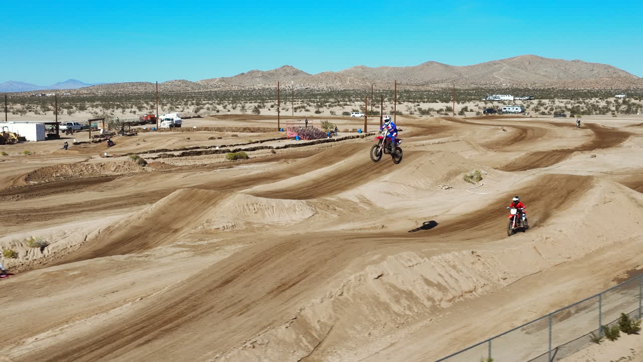 하나를 경주하는 오토바이 운전자는 비포장 경마장에서 다른 하나를 뛰어넘어 선두를 차지합니다 - 조감도