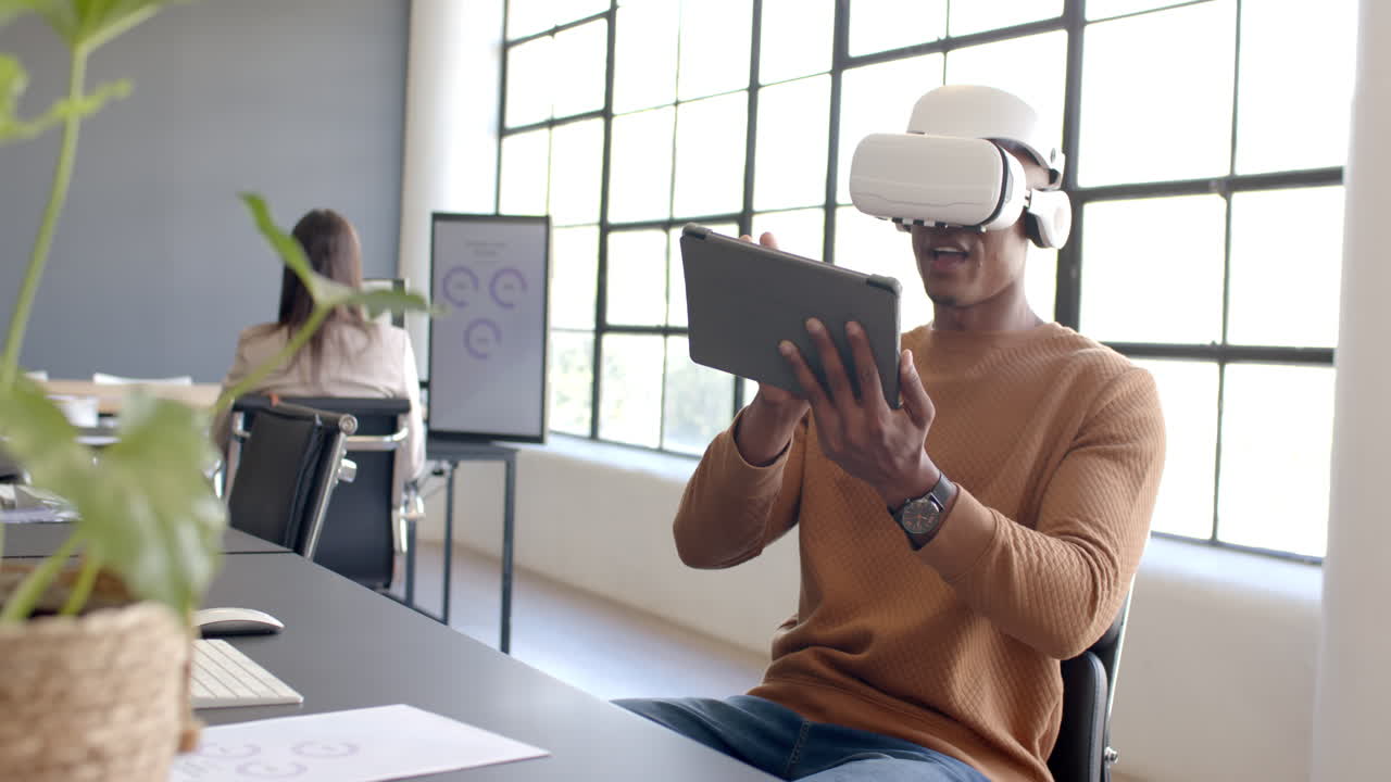 Using VR headset, African American man interacting with tablet in modern office setting