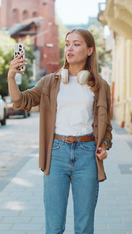 cheerful caucasian woman blogger taking selfie on smartphone talking video call on city street