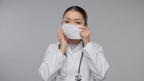 Glückliche-Asiatische-Ärztin-Zeigt-Medizinische-Maske.Medizin-,-Berufs--Und-Gesundheitskonzept-–-Videoporträt-Einer-Glücklich-Lächelnden-Asiatischen-Ärztin-Im-Weißen-Kittel-Mit-Stethoskop,-Die-Zeigt,-Wie-Man-Eine-Medizinische-Maske-Auf-Grauem-Hintergrund-Verwendet